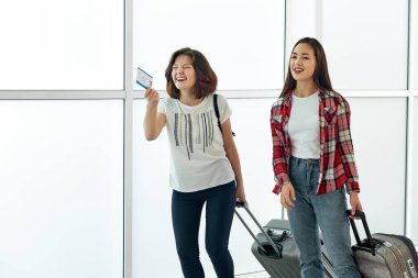 Kalkıştan önce havaalanında bavulları ve biletleri olan iki neşeli kadın. Tatilden ve seyahatten önce konuşmak ve gülmek