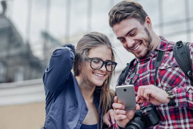 Akıllı telefonu olan mutlu bir çift. Dışarıda birlikte durup cep telefonuna bakan mutlu genç çift.