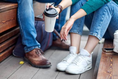 Ahşap bankta oturan kot pantolonlu bir çift. Sadece bacakları ve vücudu gösterilir..