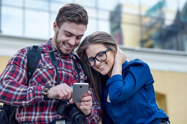 Pareja feliz con teléfono inteligente. Feliz joven pareja amorosa de pie al aire libre juntos y mirando el teléfono móvil juntos — Foto de Stock