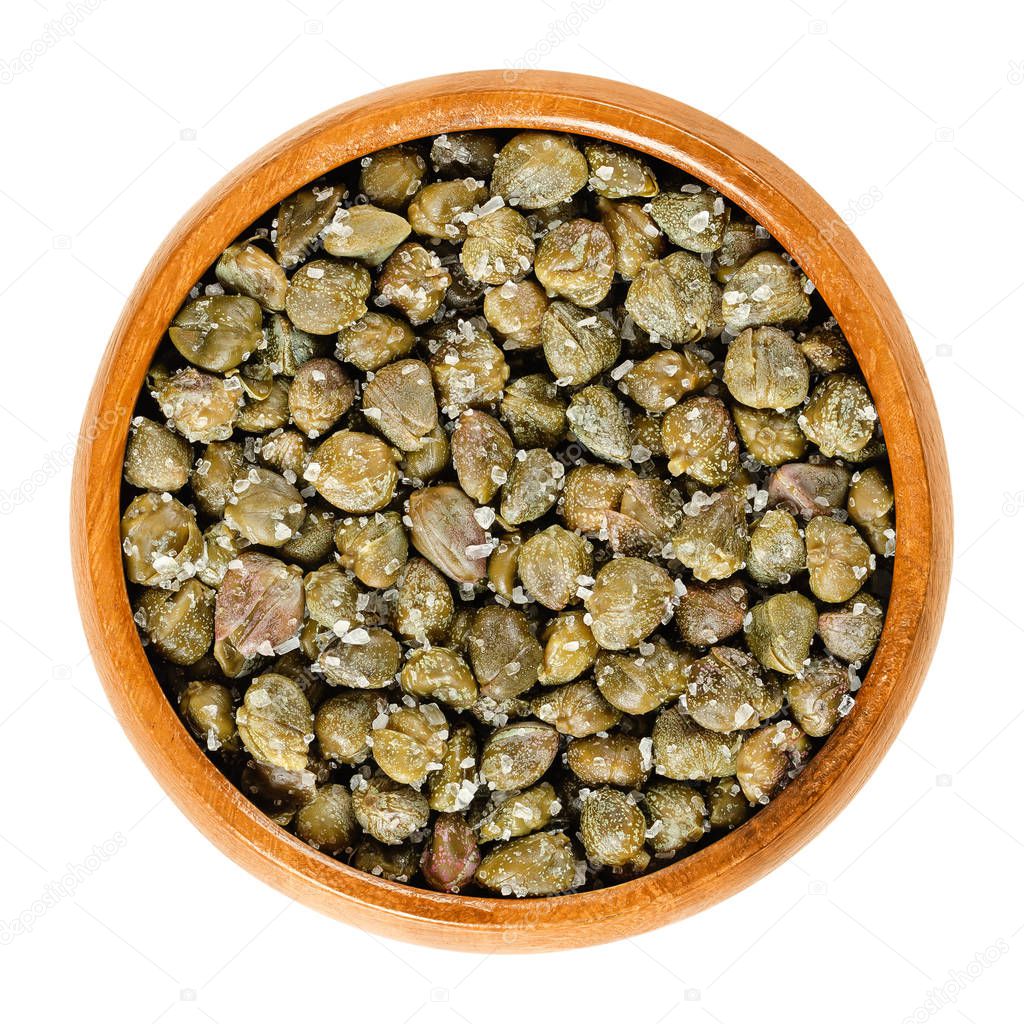 Salted capers in wooden bowl. Green, dried, pickled in sea salt, used as seasoning or garnish. Flower buds, capparis spinosa, caper bush, Flinders rose. Macro food photo closeup from above over white.