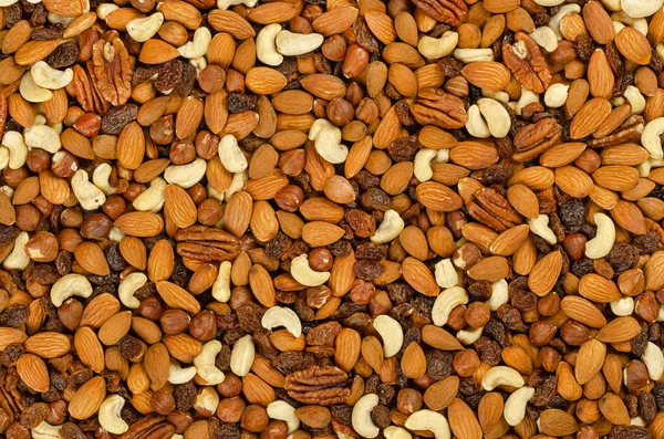 Nuts and raisins, surface and background. Snack mix of dried almonds, cashews, hazelnuts, pecans and raisins. Trail mix, student food or fodder. Raw, organic, vegan. Food photo, closeup, from above.