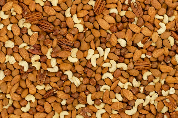 Mixed nuts, surface and background. Snack mix of dried almonds, cashews, hazelnuts and pecans. Trail mix, student food or fodder. Edible, raw, organic and vegan. Macro food photo, closeup, from above.
