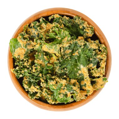 Homemade kale chips in wooden bowl. Dehydrated green leaf cabbage, coated with blended spices, nuts and vegetables. Snack and potato chip substitute. Macro food photo, closeup from above, over white. clipart