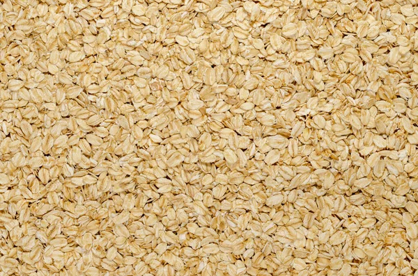 Rolled oats, surface and background. Lightly processed whole-grain food. Husked and steamed oat groats are rolled into flakes and lightly toasted to stabilize them. Food photo, top view, from above.