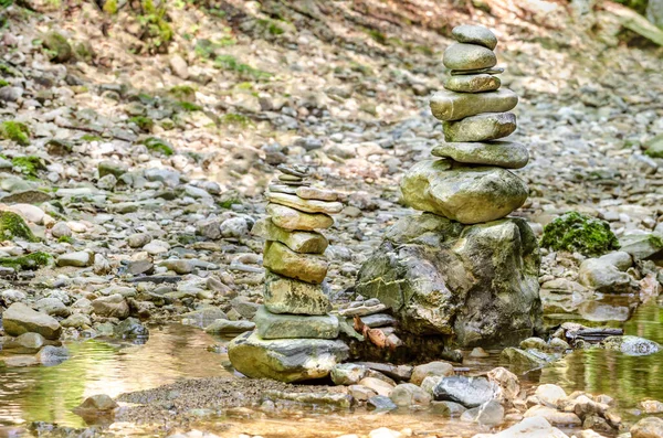 Rock balancing. Two piles of stacked rocks in a riverbed. Rocks laid flat upon each other to great height. Balanced rocks at the creek, surrounded by water, as an art form or hobby. Close-up. Photo.
