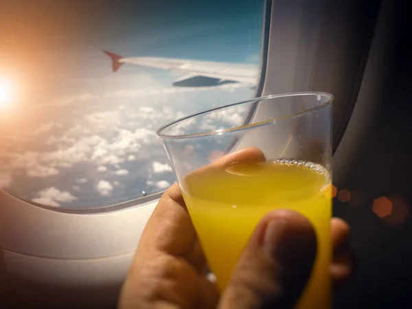 male hand holding glass of orange juice near the window of airpl