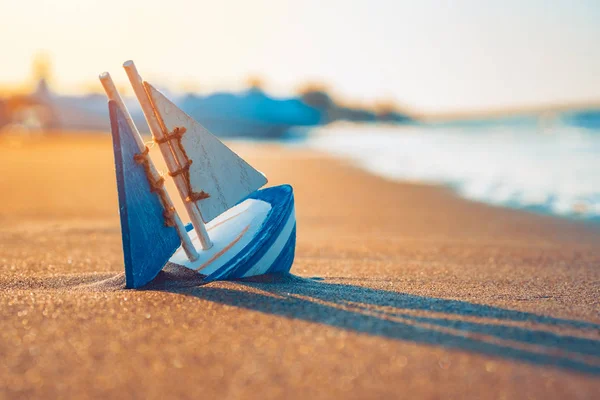 Juguete de madera velero enterrado en la arena cerca de la orilla del mar —  Fotos de Stock