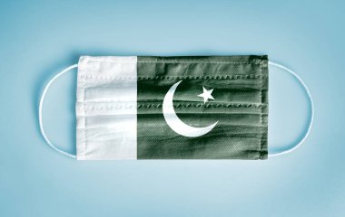 Covid-19 Coronavirus protection concept: Medical disposable face mask with Pakistan flag on blue background. WHO recommends social distancing and usage of mask to prevent from Coronavirus.  clipart