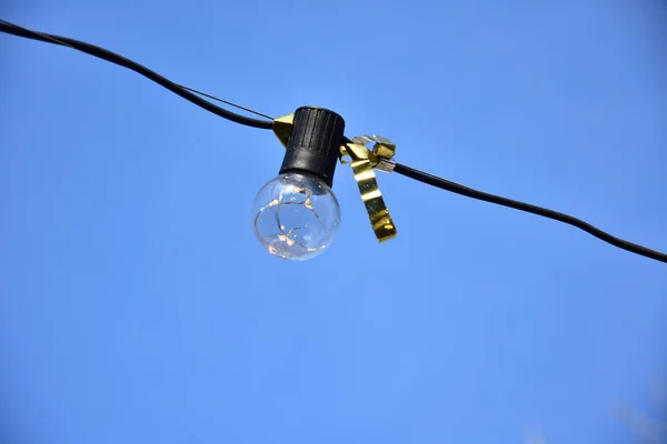 Festival glass light bulb with golden ribbon on a wire against bright blue sky