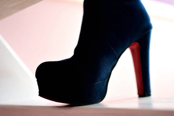 Female leg in blue high heeled boot with red sole is standing on white stairs, side view