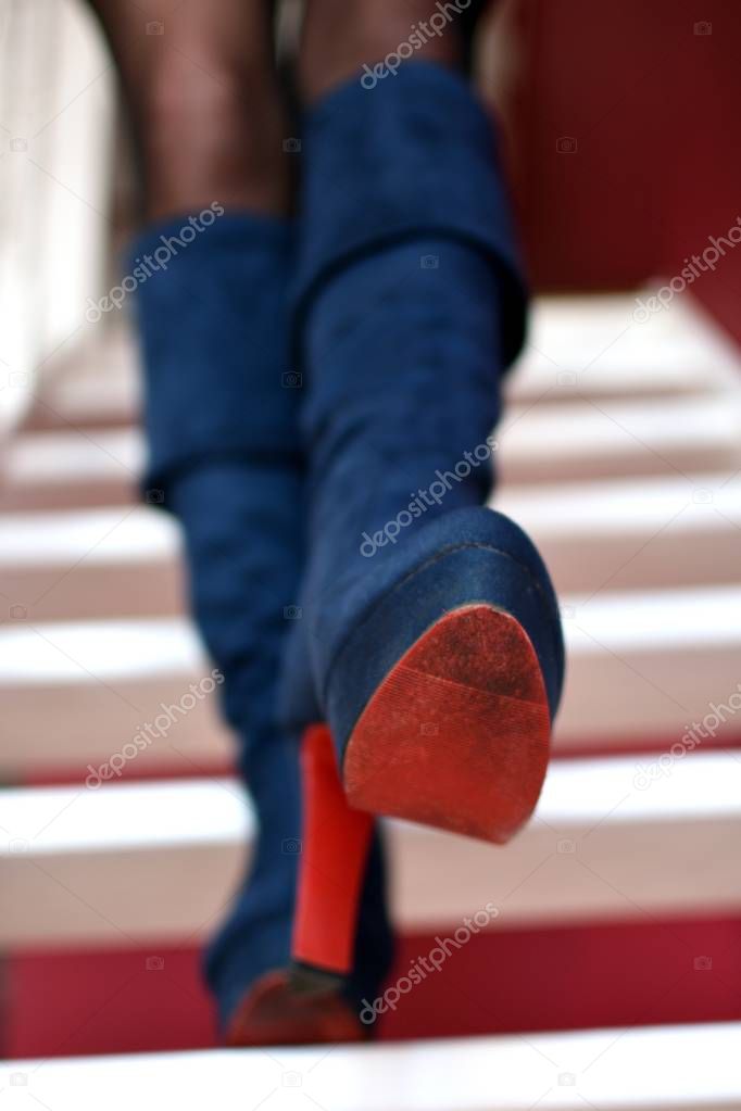 Female legs in blue high heeled boots with red soles are stepping down white stairs, front view 