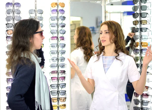 young pretty woman is trying sun glasses on at an eyewear shop with help of a shop assistant, low depth of field