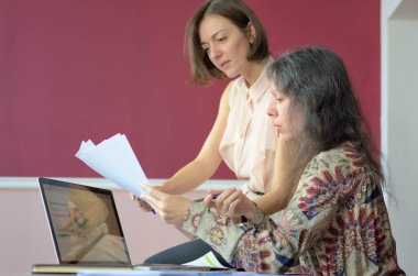 iki rahat giyimli genç bayan modelleri bir vintage ofiste bir masada oturup model serbest bırakma belgeleri, grup portre ve yakın çekim tartışmak