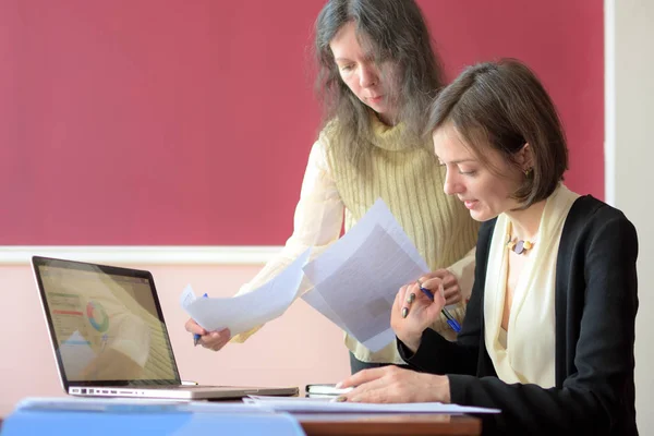 Joven dama elegantemente vestida ayuda a otra joven a trabajar con documentos, llenar formularios y firmar. Se sientan juntos en una oficina de estilo vintage en un escritorio vintage — Foto de Stock