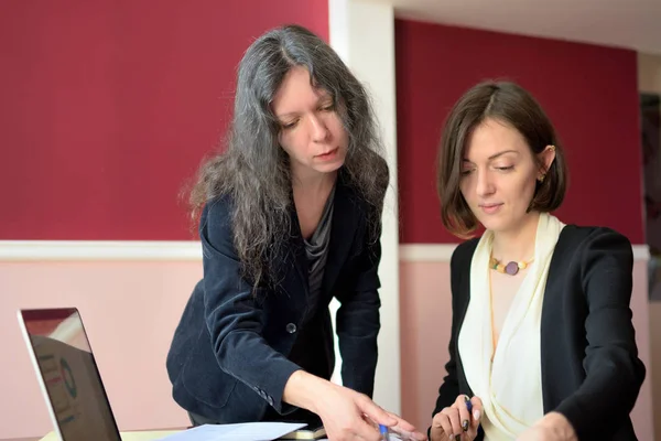 Joven dama elegantemente vestida ayuda a otra joven a trabajar con documentos, llenar formularios y firmar. Se sientan juntos en una oficina de estilo vintage en un escritorio vintage — Foto de Stock