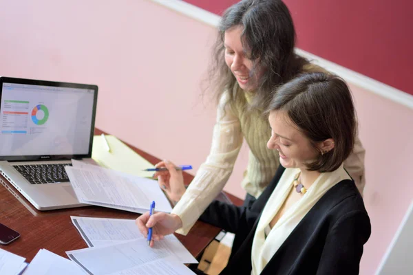 young smartly dressed lady helps another young lady to work with documents, fill forms and sign in a vintage style office at a vintage desk, overhead camera view