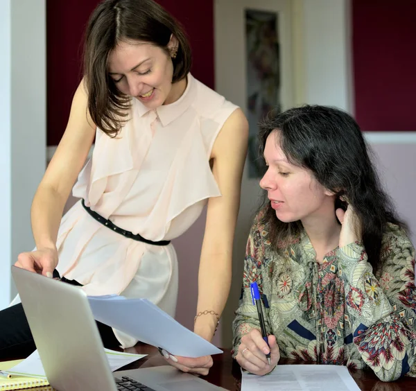 Dos modelos de damas jóvenes casualmente vestidas se sientan en un escritorio en una oficina vintage y discuten documentos de lanzamiento de modelos, retrato de grupo y primer plano Imagen De Stock