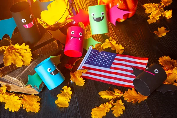 Halloween in USA. Multicolored cardboard bats. The USA flag on a wooden table. Table covered with yellow oak leaves. Old books on the table with yellowed oak leaves.