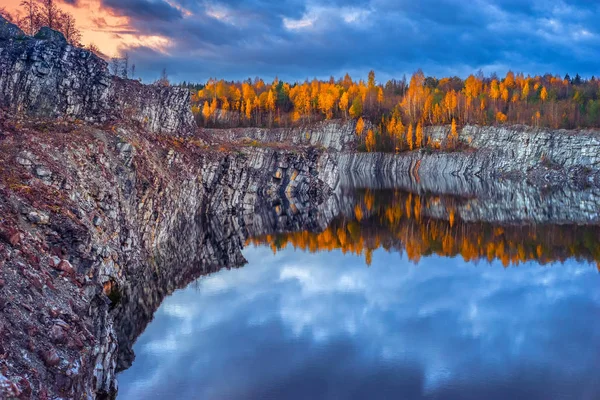The shore of the lake with rocks. Rocky shore of the lake. Autumn forest is reflected in the lake water. Autumn nature. Autumn trees on the edge of the lake.