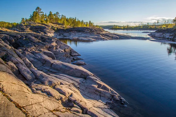 Russia. Karelia. Mirror reflection in water. Stones in the water. Rocky coast of the island. Pine trees grow on a stony shore. Nature of Karelia. — Stock Image Russia Karelia Mirror Reflection Water Stones Water Rocky Coast Island Royalty Free Stock Images