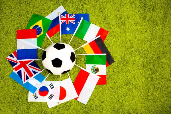 A soccer ball is surrounded by flags of countries. Countries playing football. the ball lies on the grass. Sports games of different countries. International football games.