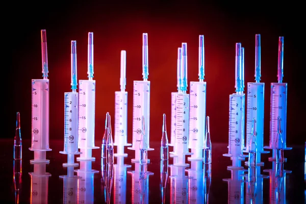 Syringes on a red background. Medical equipment. Vaccination of the population. Syringe with a needle. Ampoules with vaccines. Medical services