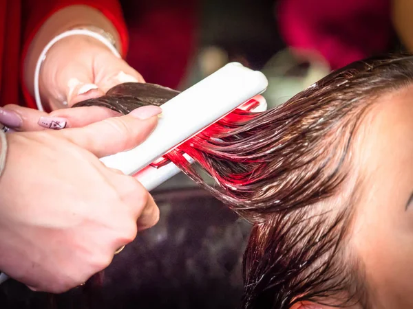 Hair dyeing in red with the help of ironing. Barber shop. Fashionable dyeing. Stylish hairstyle. Equipment for beauty salons. Hairdresser at work.