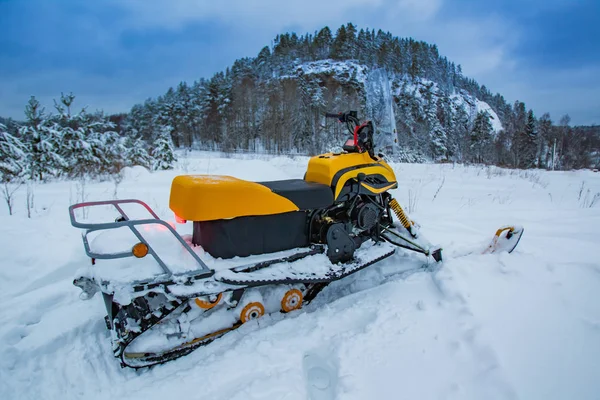Russia. Russian winter. Outdoor recreation. Winter extreme on the snowcat. Snowmobile in a field. Black and yellow ATV against the background of wooded mountain.