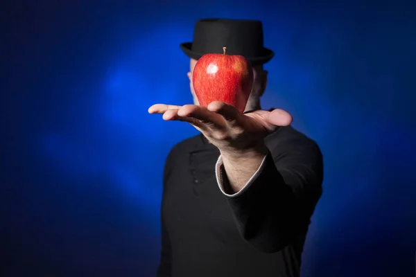 The man covered his face with an apple. The apple lies on the palm of your hand. A man in black clothes.