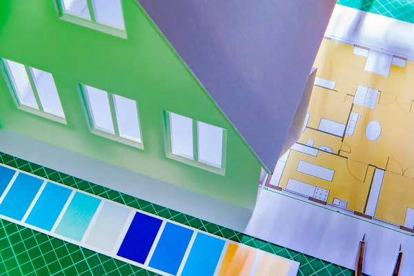 Painting works. Building design. Selection of paint for the facade. Layout of the house. Construction drawing. Architectural Studio. On the table is a house made of plastic. Paint selection