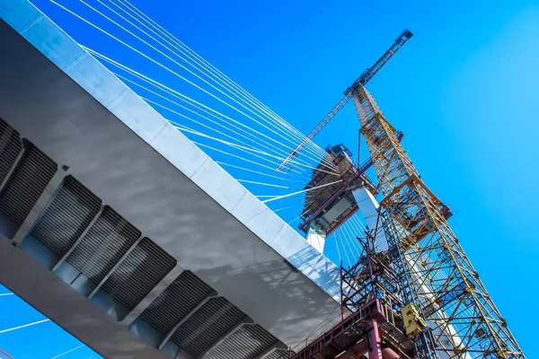 The crane lifts the load to a height. Construction of the bridge. The crane works on the construction site.