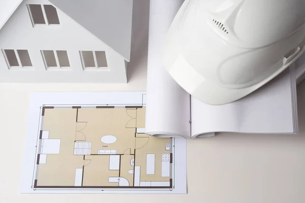 Construction concept. Construction helmet is on the table. Documentation for the construction of the cottage. Drawing cottage. Model home with documents. Architectural work.