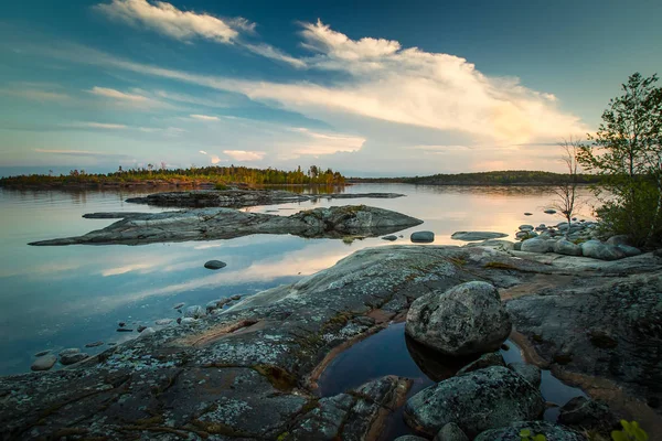 Summer sunset with reflection in water. The clouds are reflected in the water. Stones on the beach. White Nights. Karelia. Ladoga lake. — Stock Image Summer Sunset Reflection Water Clouds Reflected Water Stones Beach White Stock Photo