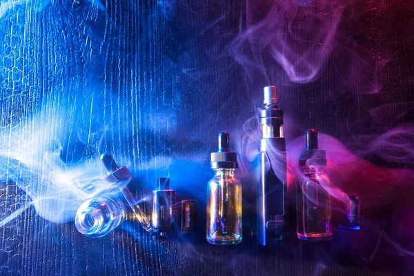 E-cigarette liquids.Vape.Accessories for Smoking. Electronic devices for Smoking.Smoking gadgets.Electronic cigarette and liquid bottles. Kit for vaping on a blue-purple background. Cigarette smoke