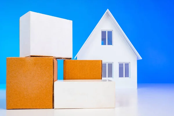 Parcels next to the layout of the house. The concept of sending at home. Delivery of parcels home. Delivery of goods to the door. Services for sending personal items. Miniature house next to the boxes