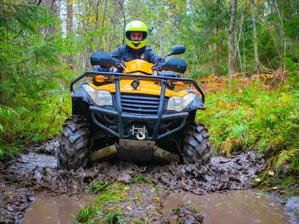 ATV racing. A man on a yellow quadrocycle. ATV tires in the mud. Man in a yellow helmet on a quad bike. A human came to the forest on an quadrocycle. ATV with a driver close-up. Extreme quad bike ride