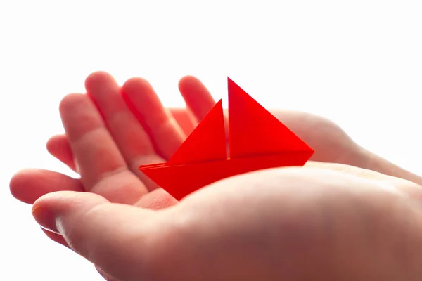 The ship in the hands. Paper ship in hands on a white background. Origami from red paper. Boat in the women\'s crayfish. Conceptual image of insurance and savings. Conceptual image of a small business.