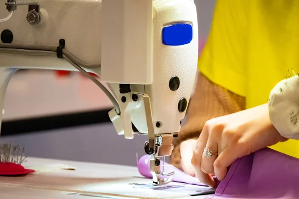 Sewing machine. A woman works on a sewing machine. A woman sews clothes. Fragment Garment Equipment. Sewing equipment. Cutting clothes. Clothes designer. Needlework. Garment factory. Tailor at work.