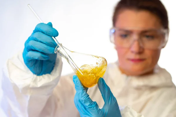 Examination of yellow chemical liquid. The girl analyzes the substance in the flask. A chemist makes a quick test of a viscous liquid. Experience in mixing different compositions.