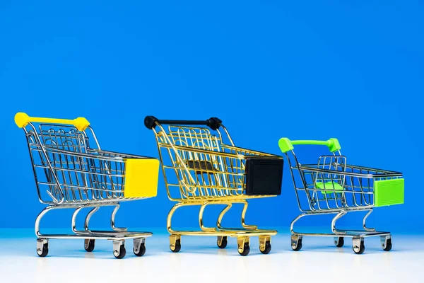 Carts for the supermarket. Concept - retail business. Miniature shopping trolleys. Shopping baskets. Carts on a blue background. Toy carts for the store. Metaphor - shopping in the store. Shop.