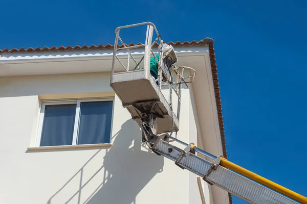 House painting. Painting the building. The painter works at height. Exterior decoration of the house. Painting the walls of the building. Special cradle for high-rise works.
