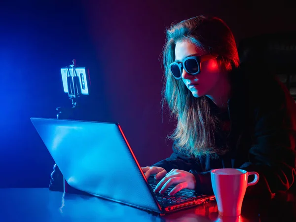 Woman web designer with laptop. Web designer works in the dark. Girl works near the computer. Woman web designer working remotely. Phone on a stand next to a laptop. Girl develops sites. UX design