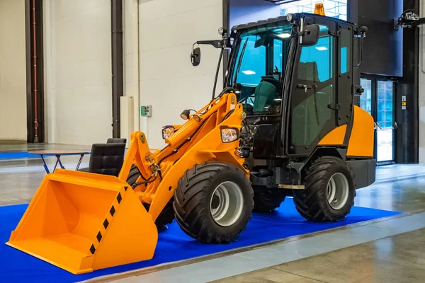 Backhoe loader. A small excavator is in the hangar. Loading equipment. Equipment for work in the warehouse. Yellow excavator in a building. Sale of street cleaning equipment.