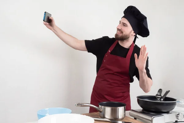 Chef takes a master class on the phone. Cooking training. Cook in a black hat. Cook is making a training video. chef kitchen takes off the recipe. Guy waves his hand. Restaurant chef takes a selfie