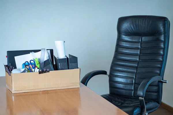 Dismissal. Fired businessman box on office desk. Box with office things a symbol of dismissal. Dismissed from work. Empty office chair. Concept - last working day. Company staff reduction. Cardboard