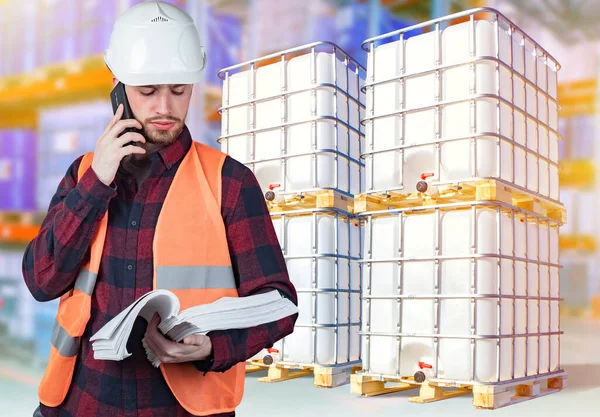 Warehouse of chemical products. Storage of tanks with chemical liquids. A storekeeper with documents in hand is talking on a mobile phone. Warehouse business.