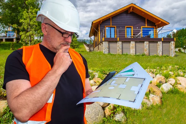 A man with construction documents in his hands on the background of the cottage. Construction of country houses on individual projects. Engineering support. Work of an architect.