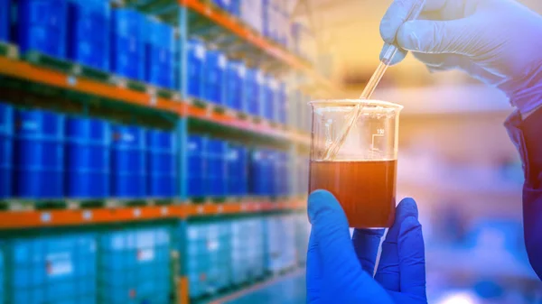 Jar with dark liquid in the hands of a laboratory assistant. Concept - refining industry. Chemist checks oil before exporting. Hands of a chemist on the background of shelving with petroleum products