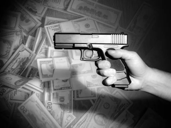 Hand with a gun on a background of money. Concept - crimes committed for the sake of money. Gun as a symbol of murder. Concept - attacks due to job loss. Growth of crime due to unemployment. Killer